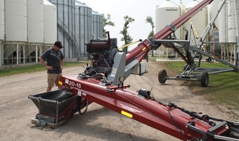 Farmer staning next to a grain auger. 