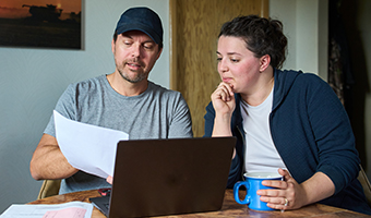 Two farmers in discussion with papers and a laptop on the table